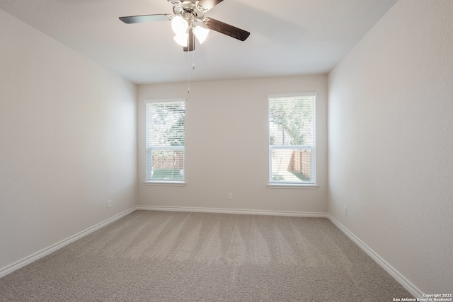 spare room with a wealth of natural light, light colored carpet, ceiling fan, and baseboards