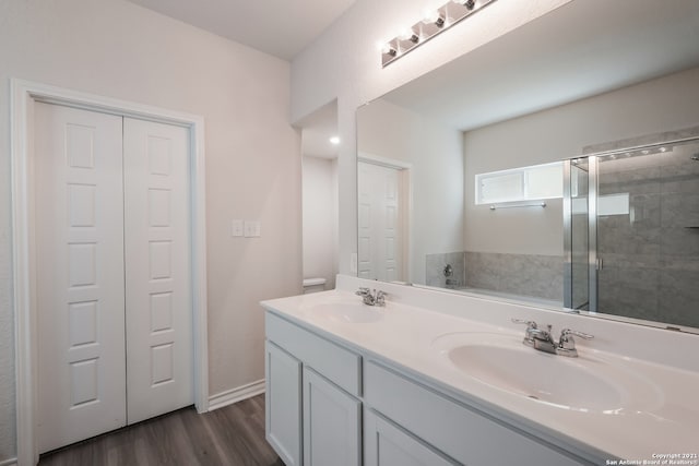 bathroom with a stall shower, double vanity, a sink, and wood finished floors