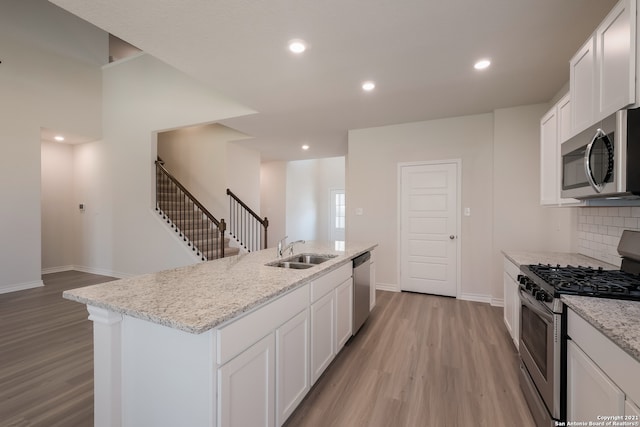 kitchen featuring a kitchen island with sink, stainless steel appliances, a sink, backsplash, and light wood finished floors