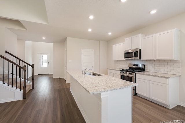 kitchen with a kitchen island with sink, a sink, appliances with stainless steel finishes, tasteful backsplash, and dark wood finished floors