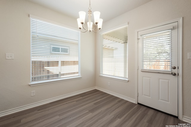 unfurnished dining area with dark wood finished floors, baseboards, and an inviting chandelier