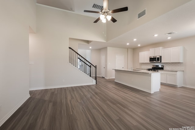 kitchen with white cabinets, appliances with stainless steel finishes, dark hardwood / wood-style flooring, ceiling fan, and a center island with sink