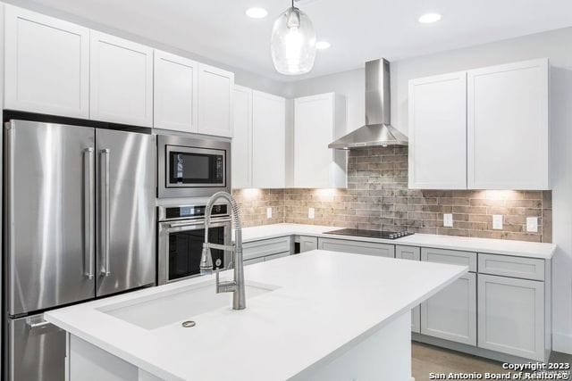 kitchen featuring stainless steel appliances, a center island with sink, wall chimney exhaust hood, and tasteful backsplash