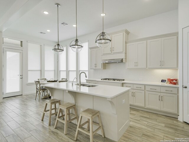 kitchen with a kitchen island with sink, wall chimney exhaust hood, decorative light fixtures, backsplash, and sink