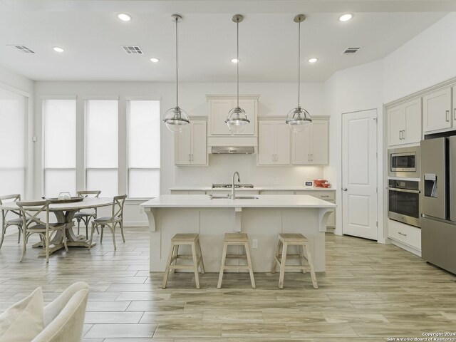 kitchen with an island with sink, light wood-type flooring, hanging light fixtures, a breakfast bar area, and appliances with stainless steel finishes