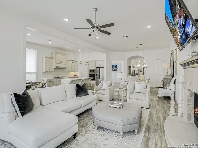 living room featuring ceiling fan with notable chandelier, light hardwood / wood-style floors, and a fireplace