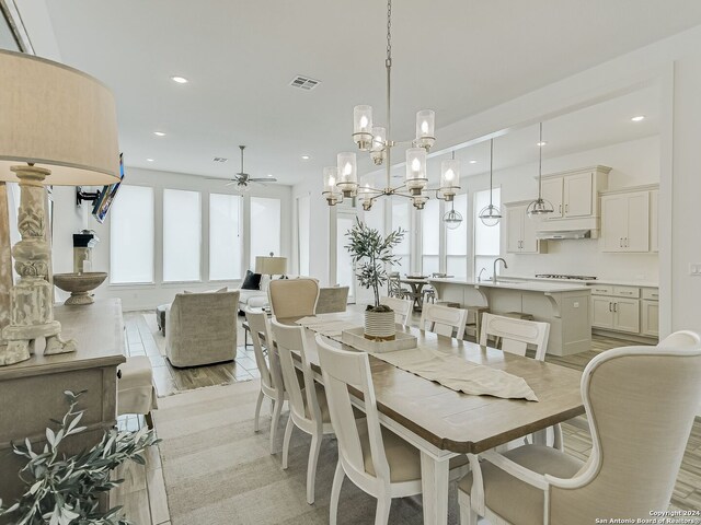 dining area featuring ceiling fan with notable chandelier, a healthy amount of sunlight, sink, and light hardwood / wood-style flooring