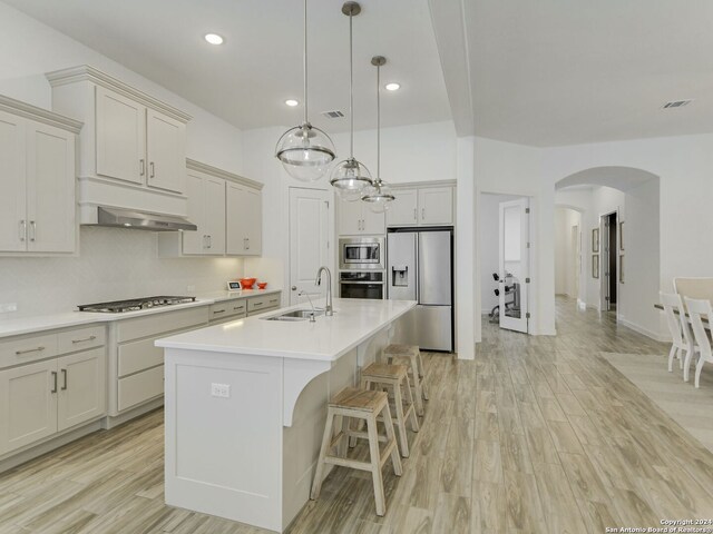 kitchen featuring light hardwood / wood-style flooring, hanging light fixtures, sink, a kitchen island with sink, and appliances with stainless steel finishes