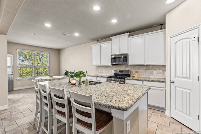 kitchen featuring appliances with stainless steel finishes, white cabinetry, light stone counters, and a center island with sink