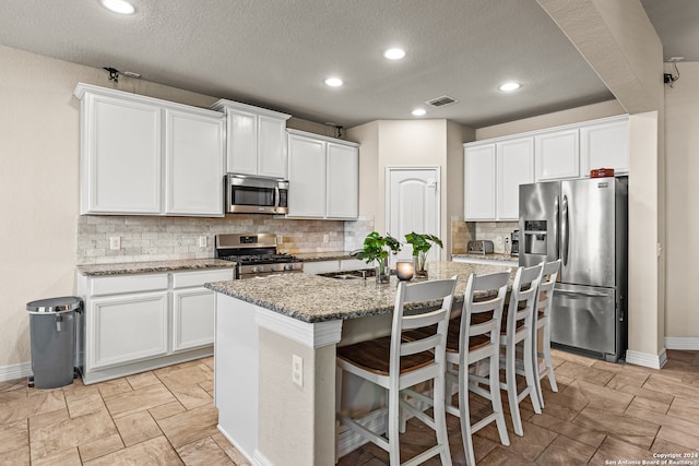 kitchen featuring appliances with stainless steel finishes, decorative backsplash, white cabinetry, and a center island with sink