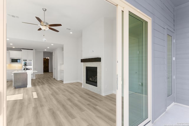 unfurnished living room with light hardwood / wood-style floors, wood walls, sink, and ceiling fan