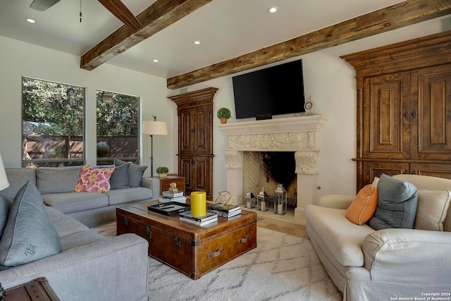 living room featuring beam ceiling, light hardwood / wood-style floors, a fireplace, and ceiling fan