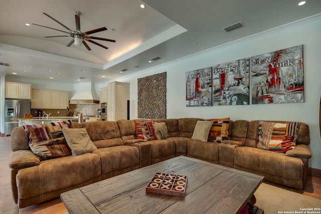 living room with crown molding, a tray ceiling, light hardwood / wood-style floors, and ceiling fan