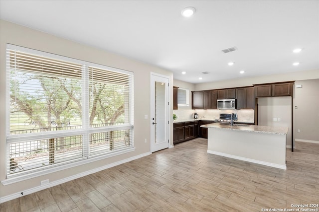 kitchen featuring light stone counters, an island with sink, dark brown cabinets, appliances with stainless steel finishes, and sink