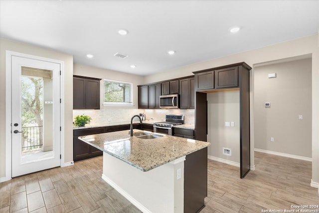 kitchen featuring tasteful backsplash, an island with sink, light stone counters, sink, and appliances with stainless steel finishes