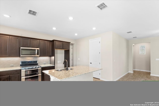 kitchen featuring light stone countertops, a center island with sink, stainless steel appliances, sink, and tasteful backsplash