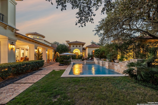 pool at dusk with a patio area and a lawn