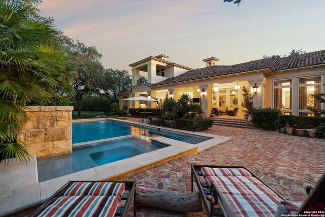 pool at dusk with an in ground hot tub and a patio