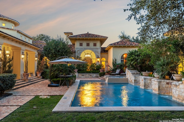 pool at dusk with pool water feature and a patio