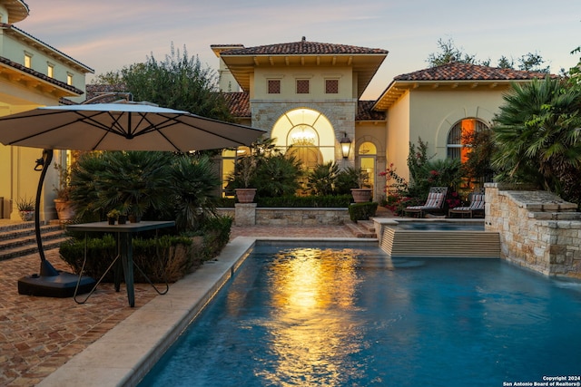 pool at dusk featuring a patio area and pool water feature