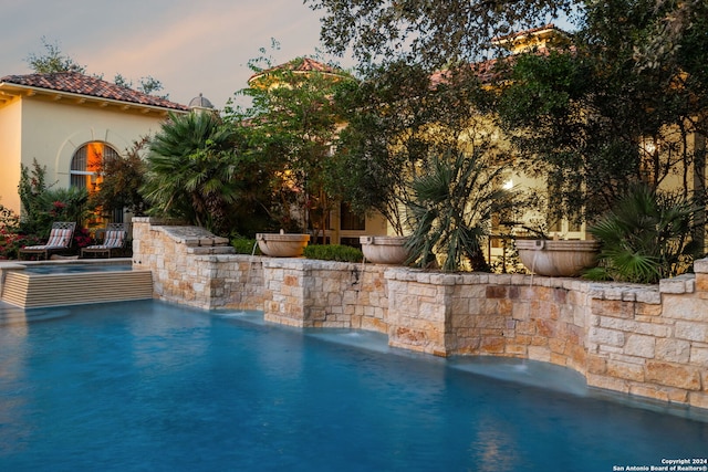 pool at dusk featuring pool water feature