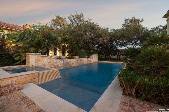 pool at dusk with an in ground hot tub