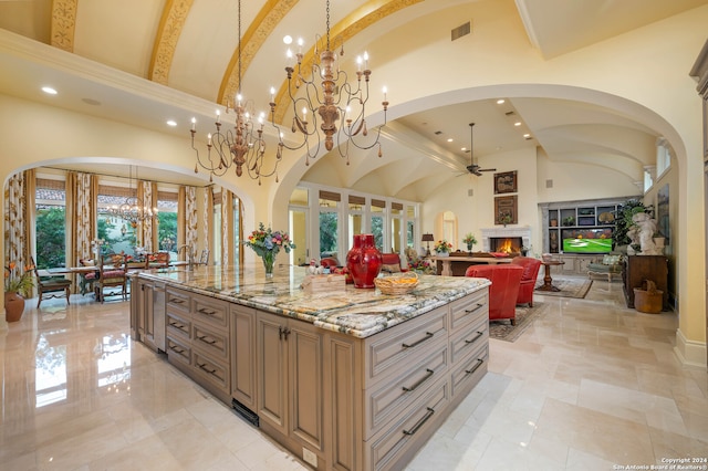 kitchen with decorative light fixtures, a spacious island, light stone countertops, and high vaulted ceiling