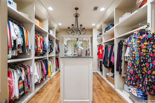 spacious closet featuring light hardwood / wood-style floors and an inviting chandelier