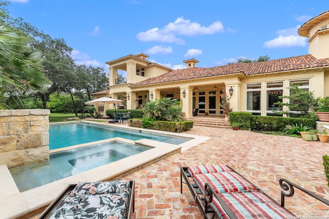 rear view of house featuring a swimming pool with hot tub, a patio area, and french doors