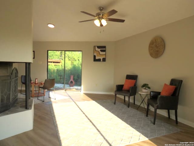 sitting room with a multi sided fireplace, ceiling fan, and wood-type flooring