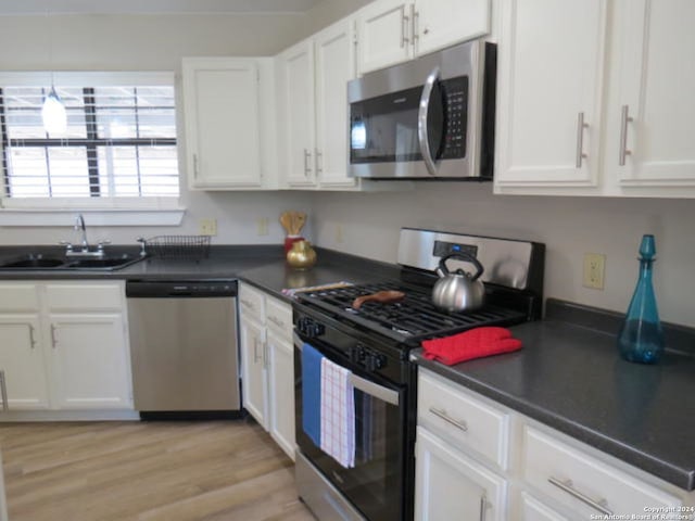 kitchen with decorative light fixtures, light hardwood / wood-style flooring, stainless steel appliances, white cabinetry, and sink