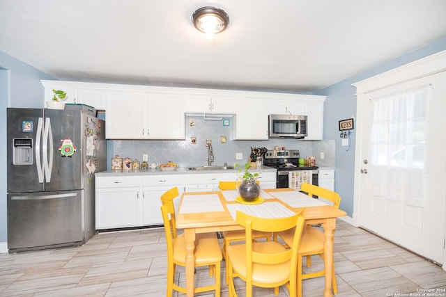 kitchen with stainless steel appliances, white cabinets, light tile flooring, and backsplash