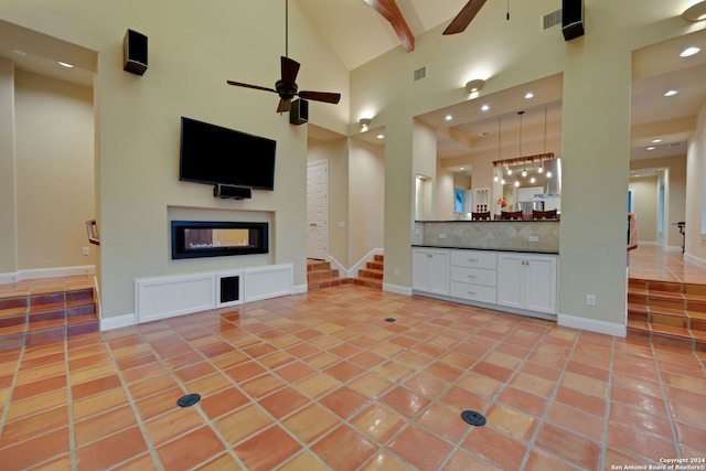 unfurnished living room featuring ceiling fan, a multi sided fireplace, beamed ceiling, tile floors, and high vaulted ceiling