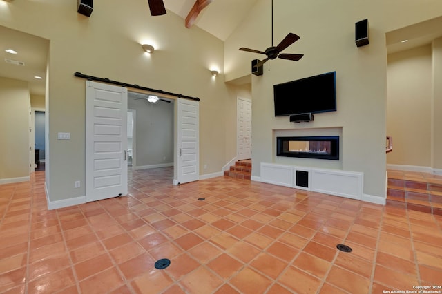 unfurnished living room with ceiling fan, a barn door, light tile floors, a multi sided fireplace, and high vaulted ceiling