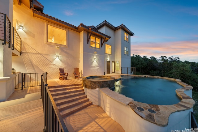 pool at dusk featuring an in ground hot tub