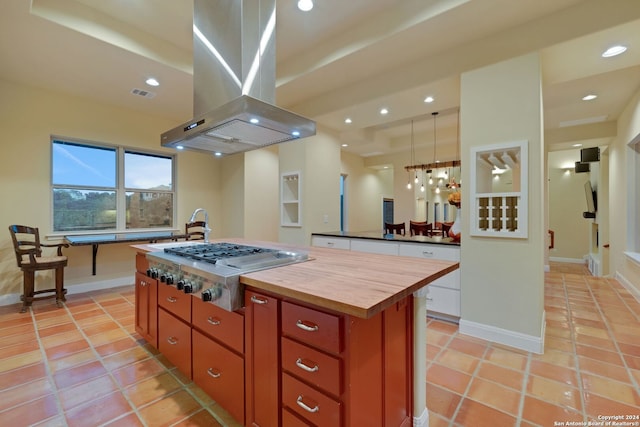 kitchen with decorative light fixtures, island exhaust hood, a kitchen island with sink, butcher block countertops, and light tile floors