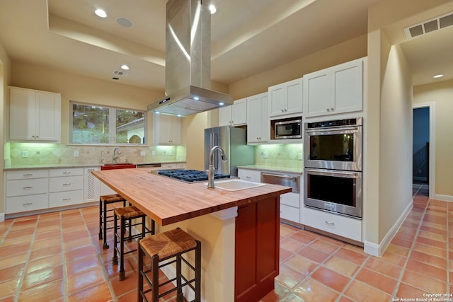 kitchen featuring backsplash, a center island with sink, island range hood, white cabinets, and appliances with stainless steel finishes