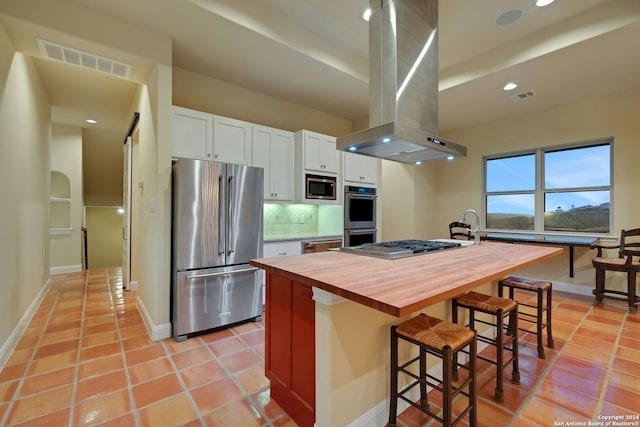 kitchen with island exhaust hood, backsplash, white cabinets, a kitchen bar, and appliances with stainless steel finishes