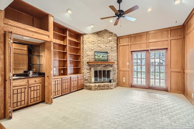 carpeted living room with wooden walls, lofted ceiling, a brick fireplace, built in features, and ceiling fan