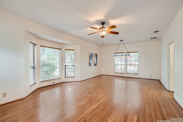 spare room with ceiling fan with notable chandelier, light wood-type flooring, and a wealth of natural light