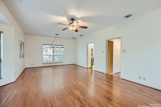 unfurnished room featuring ceiling fan with notable chandelier and light hardwood / wood-style flooring