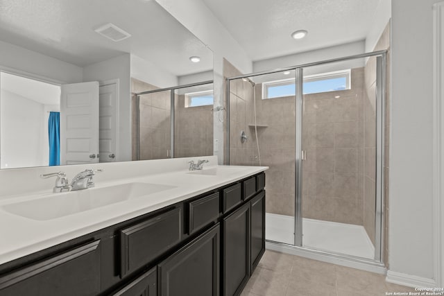 bathroom with tile floors, a shower with door, a textured ceiling, and dual bowl vanity