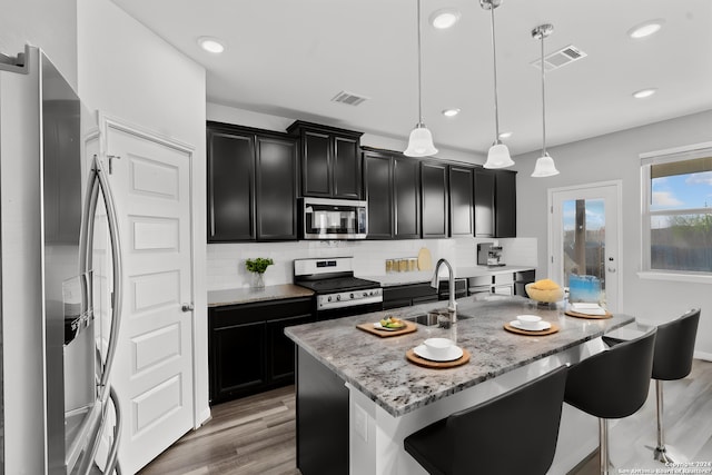 kitchen featuring stainless steel appliances, hanging light fixtures, an island with sink, and backsplash