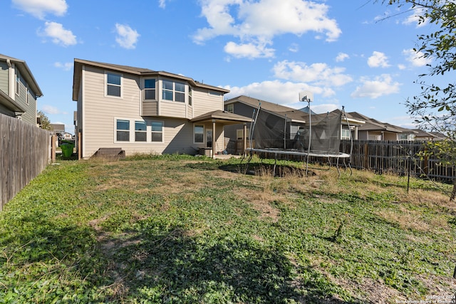 rear view of house with a yard and a trampoline