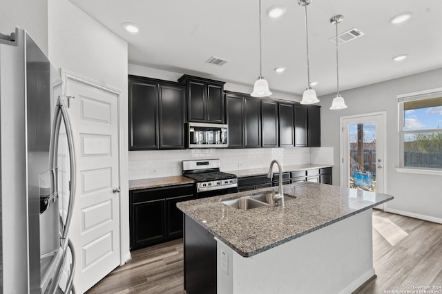 kitchen featuring stainless steel appliances, backsplash, a center island with sink, hardwood / wood-style flooring, and pendant lighting