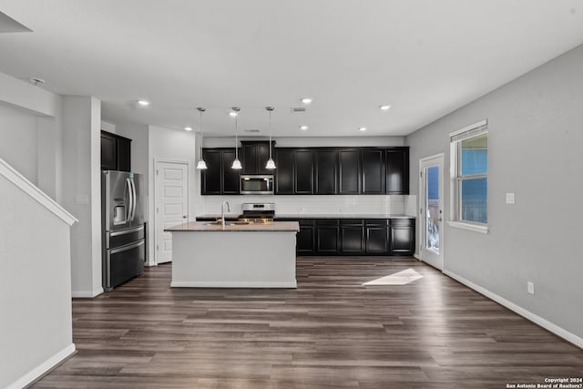 kitchen with dark hardwood / wood-style floors, a center island with sink, tasteful backsplash, and appliances with stainless steel finishes