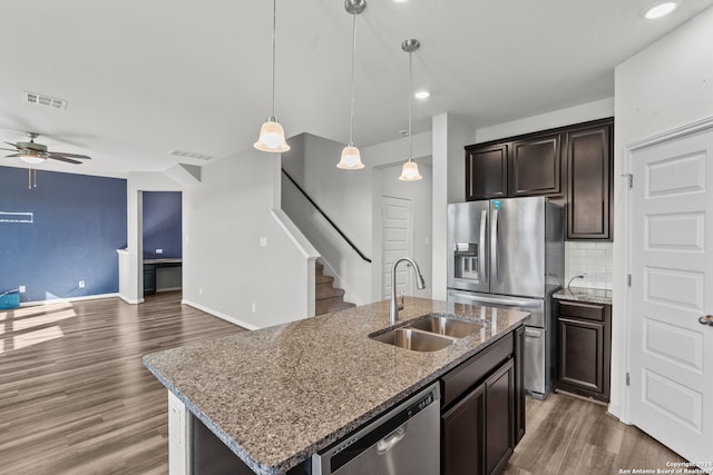 kitchen with tasteful backsplash, stainless steel appliances, a center island with sink, dark wood-type flooring, and sink