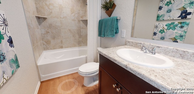 full bathroom with hardwood / wood-style floors, toilet, tiled shower / bath, and large vanity