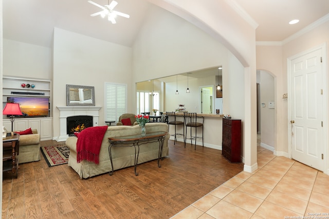 living room featuring ceiling fan, light hardwood / wood-style floors, a high ceiling, ornamental molding, and built in shelves