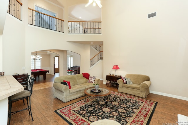 living room with a chandelier, a towering ceiling, hardwood / wood-style floors, and billiards